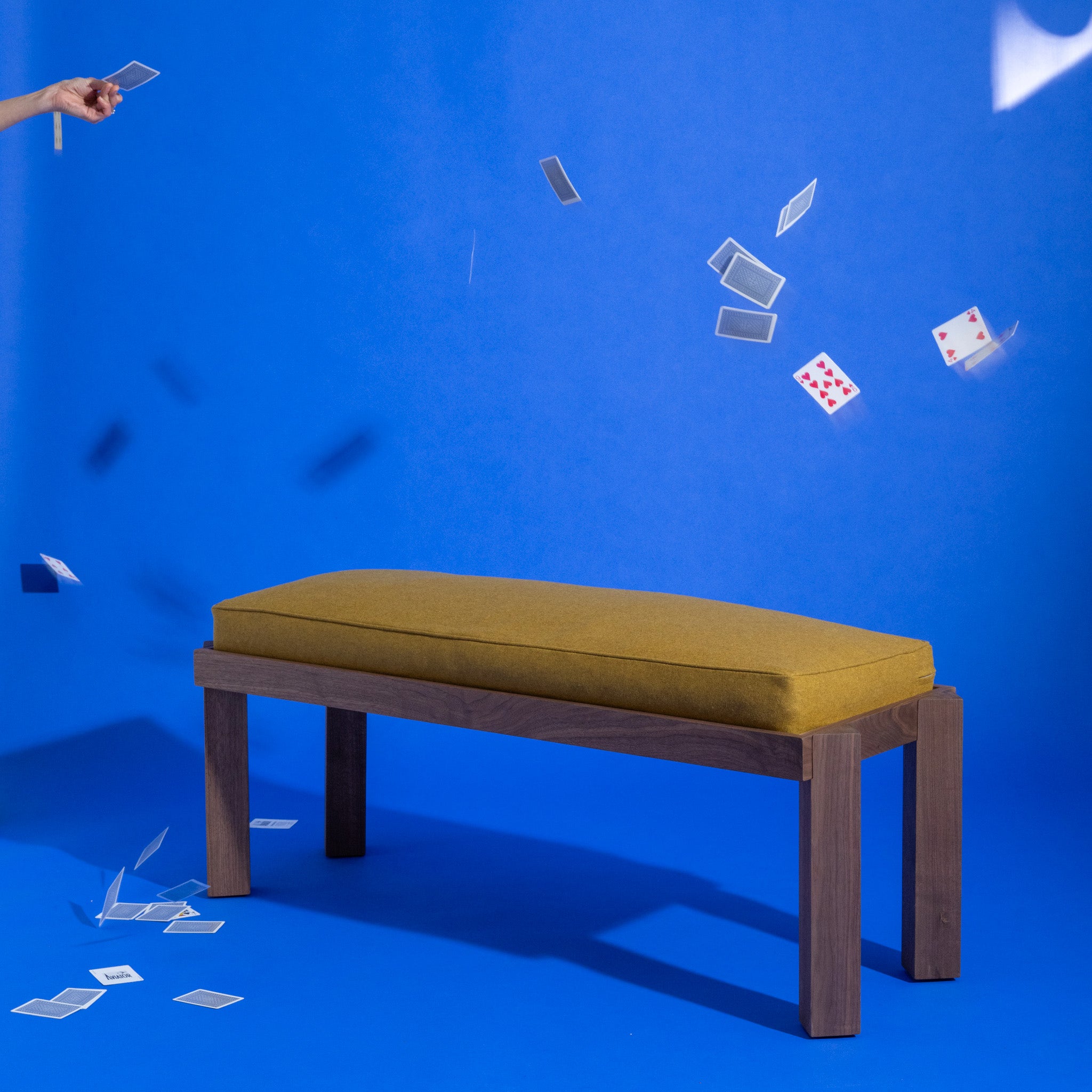 Yellow cushioned bench on a blue background with playing cards floating around.