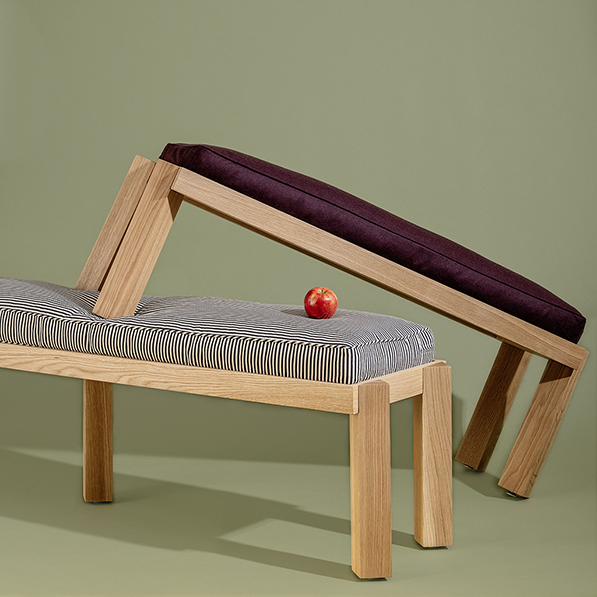 Wooden bench with striped cushion and red apple on a green background