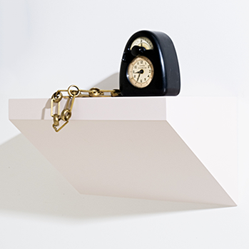 Black clock with gold chain on a wall shelf