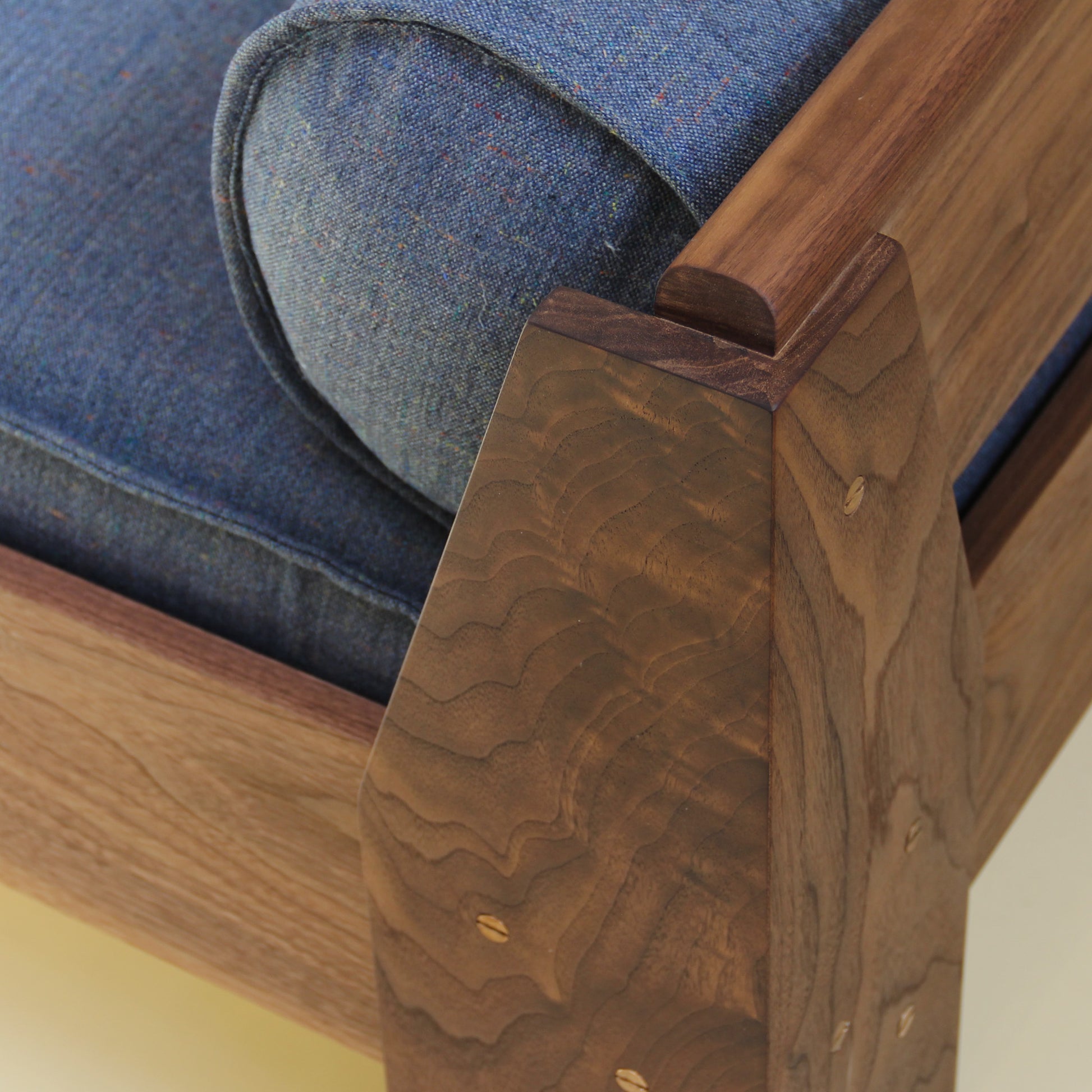 Wooden daybed with a cushion made from a wool and linen textile with a subtle denim-like texture on a plain background