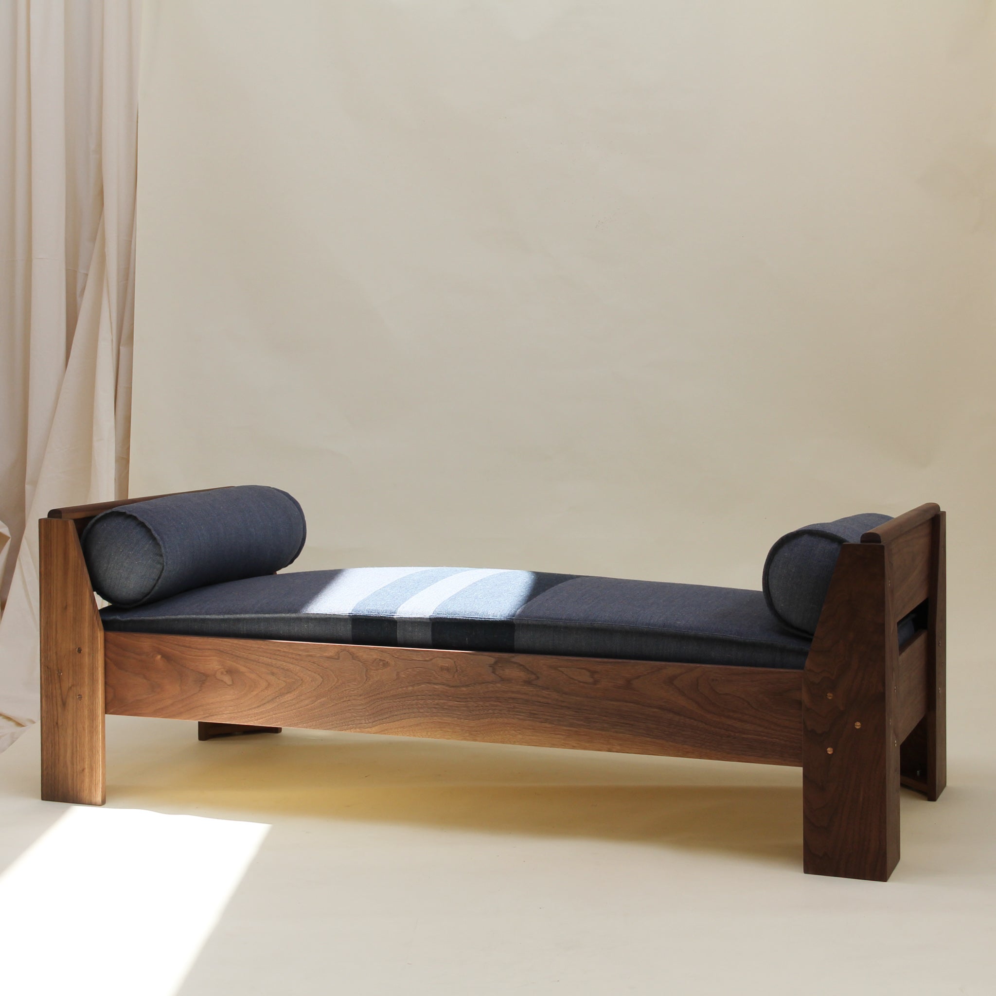 Wooden daybed with a cushion made from a wool and linen textile with a subtle denim-like texture on a plain background