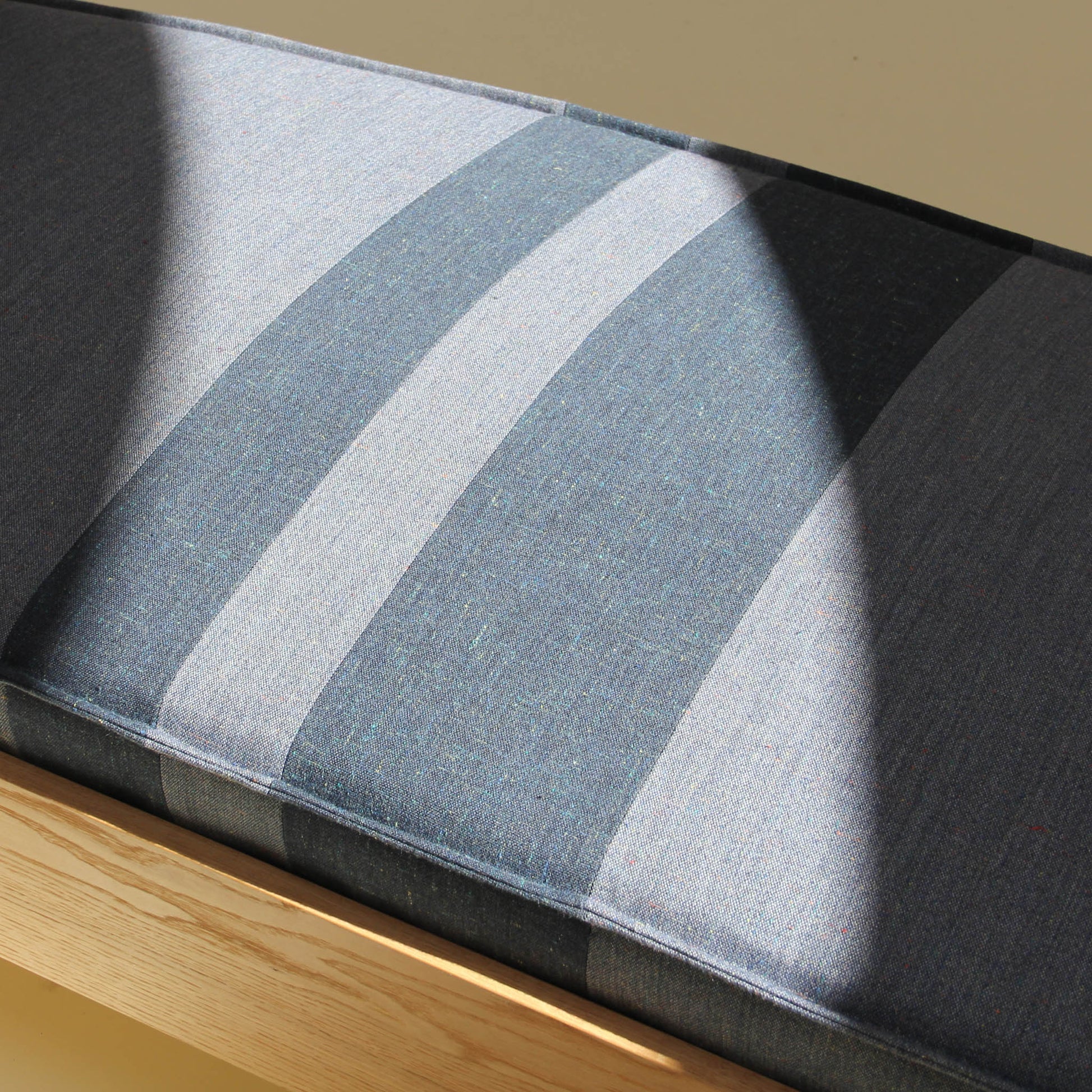 Close up of the bench cushion. The upholstery is a wool and linen textile with a subtle denim-like texture that feels relaxed and durable