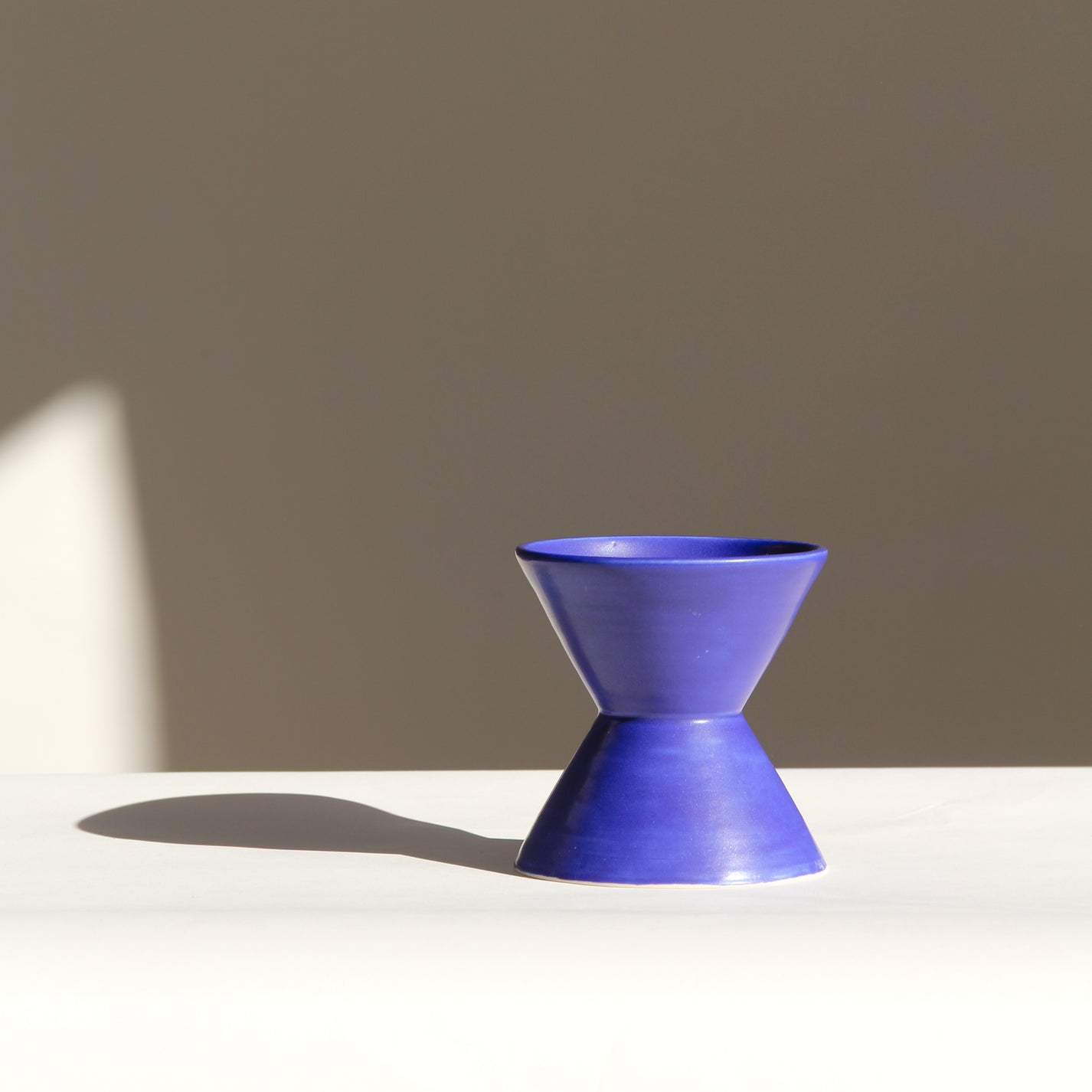 Blue ceramic vase on a white surface with a beige background