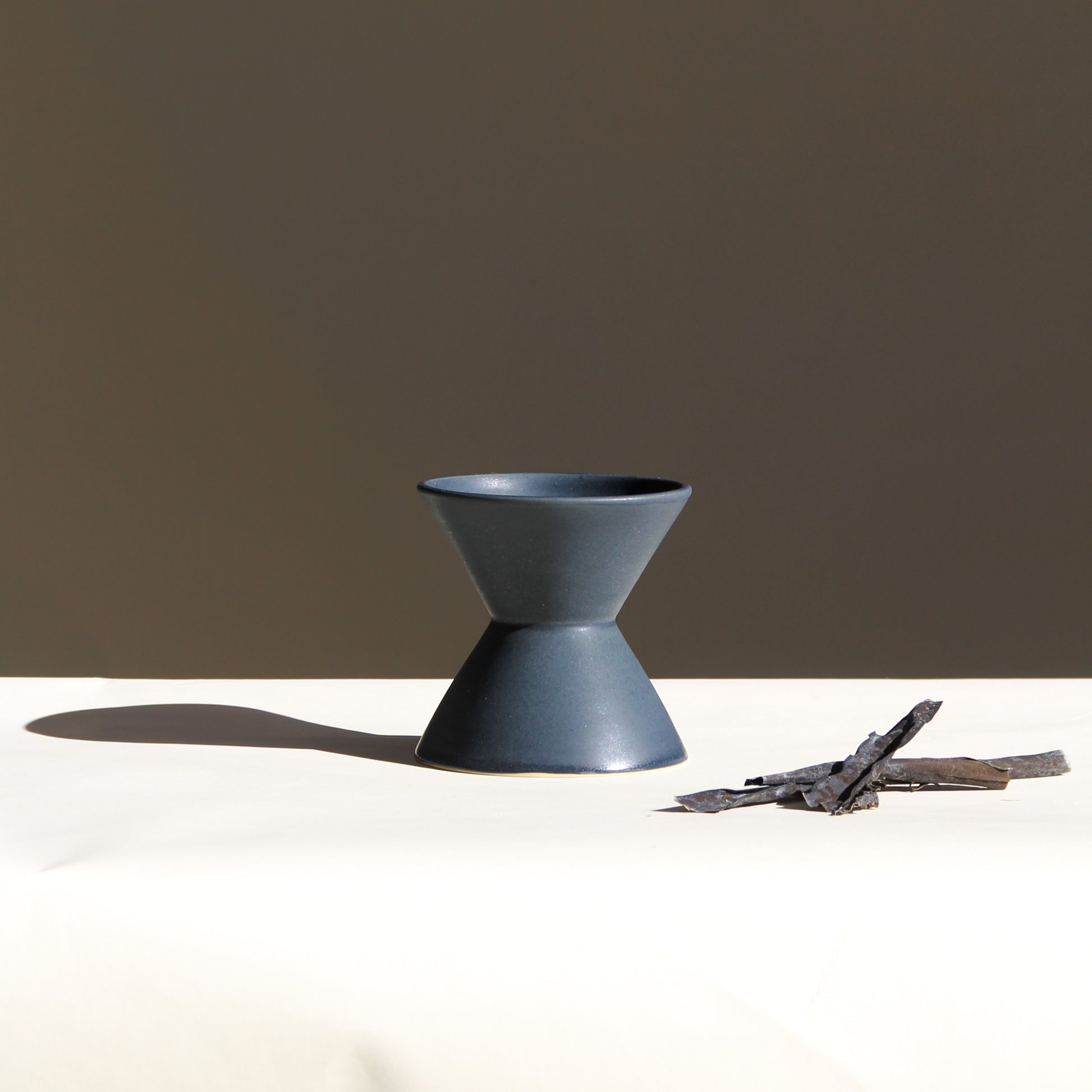 Dark grey ceramic vase on a white surface with a brown background
