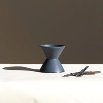 Dark grey ceramic vase on a white surface with a brown background