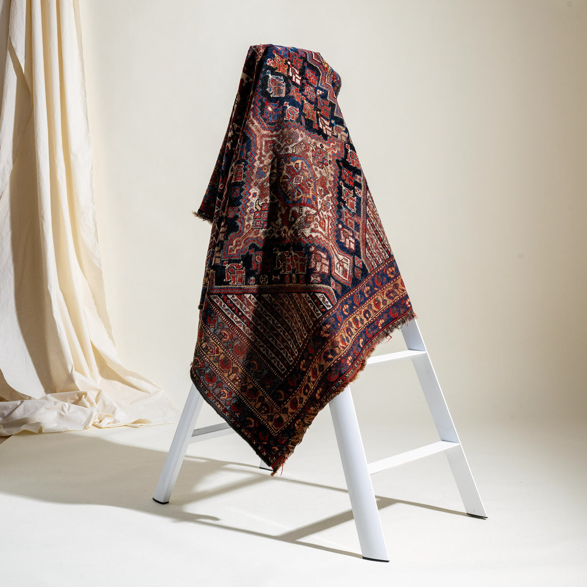 Decorative patterned blanket draped over a white ladder against a neutral background