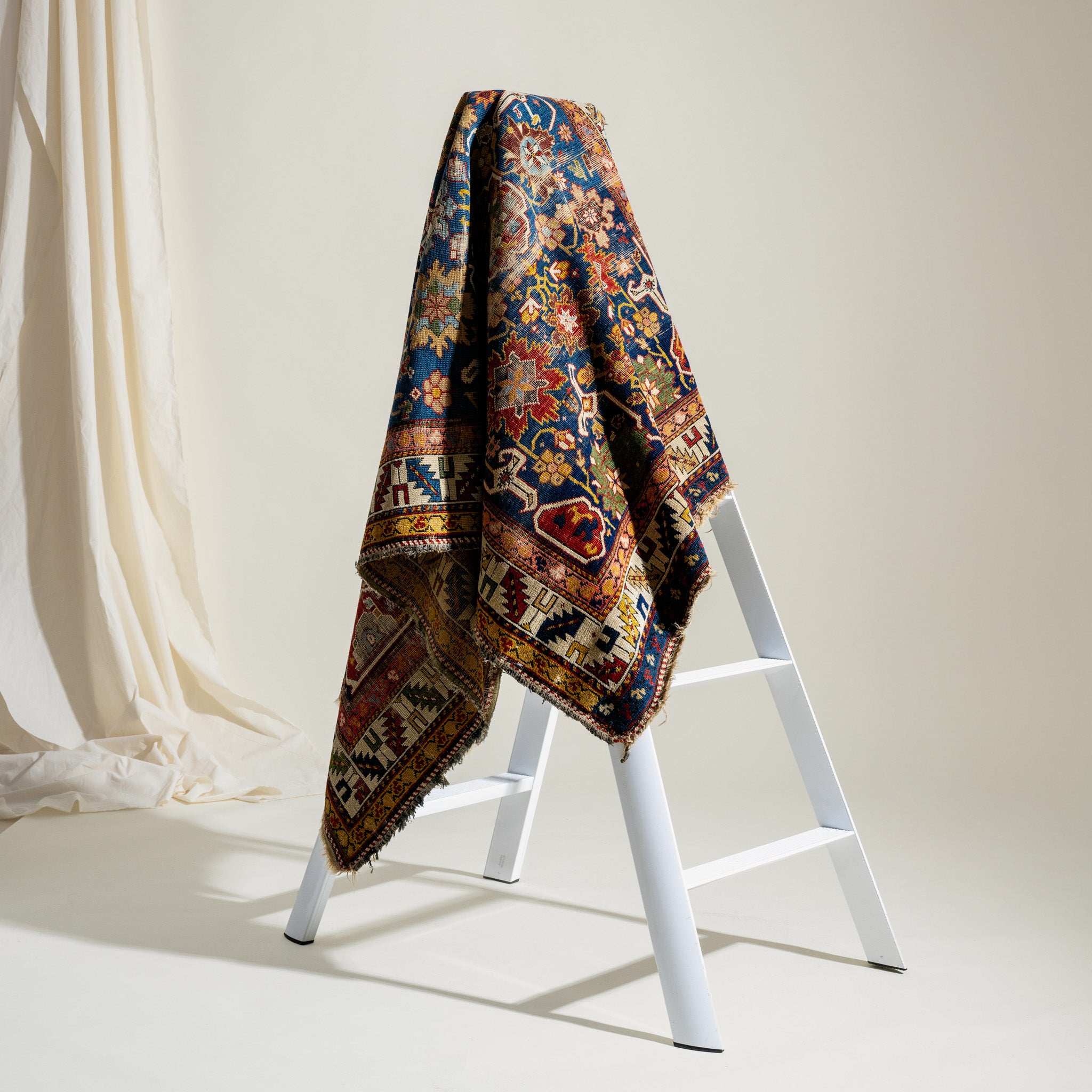 Colorful patterned rug draped over a white ladder against a neutral background