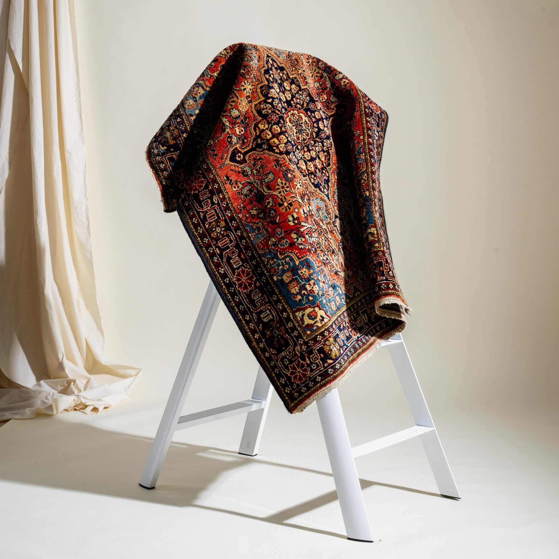 Decorative rug draped over a white ladder against a neutral background