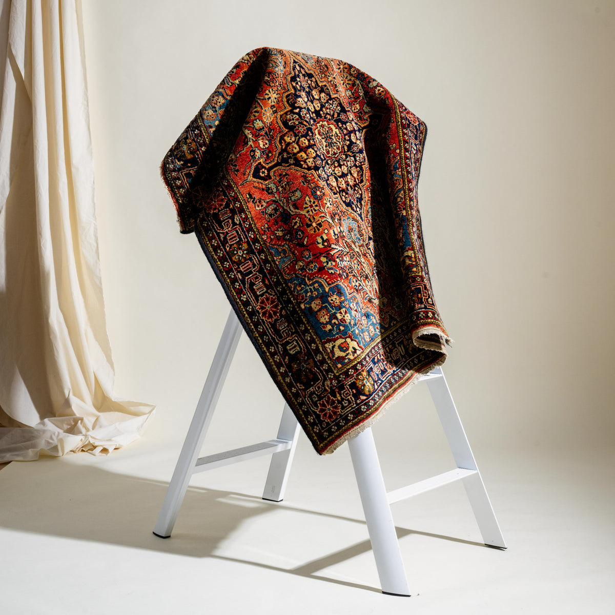 Decorative rug draped over a white ladder against a neutral background
