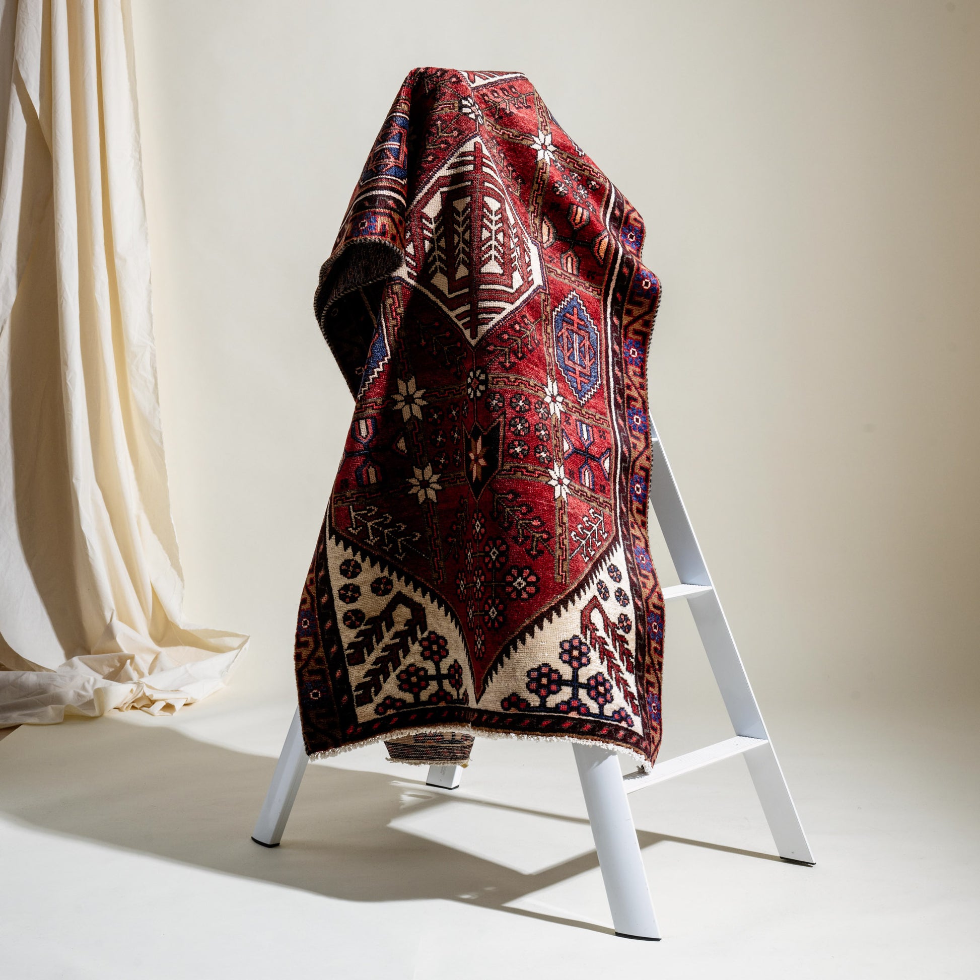 Decorative vintage red patterned rug on a white stand against a neutral background