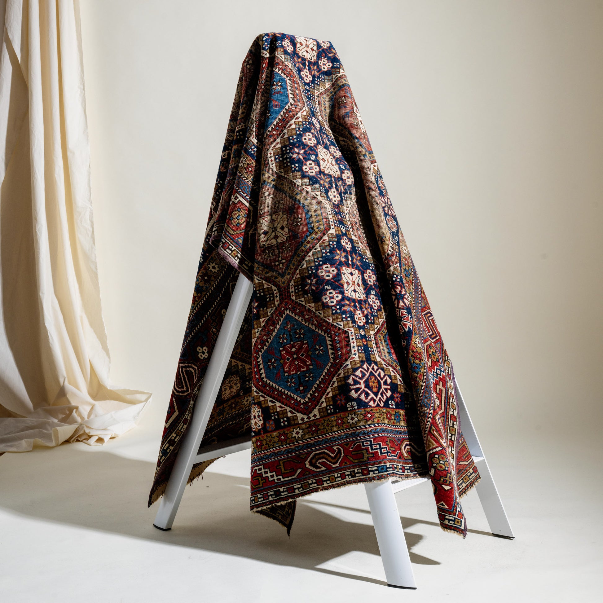 Decorative rug draped over a white ladder against a neutral background