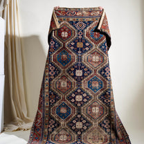 Decorative rug with intricate patterns draped held up by a person against a white wall