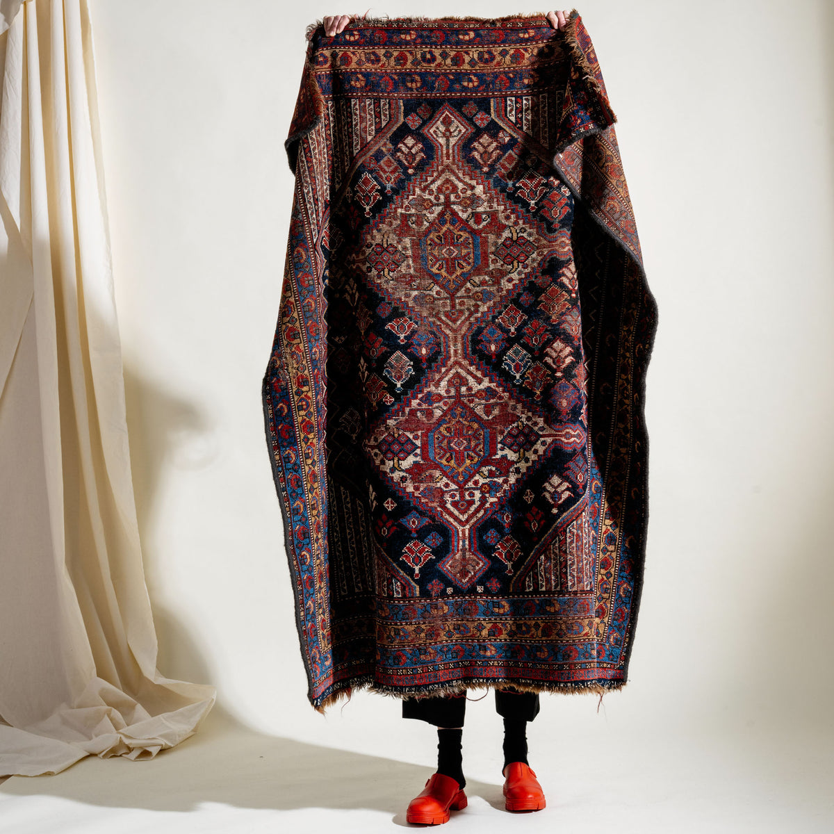 Person holding up a patterned rug over their body against a white background