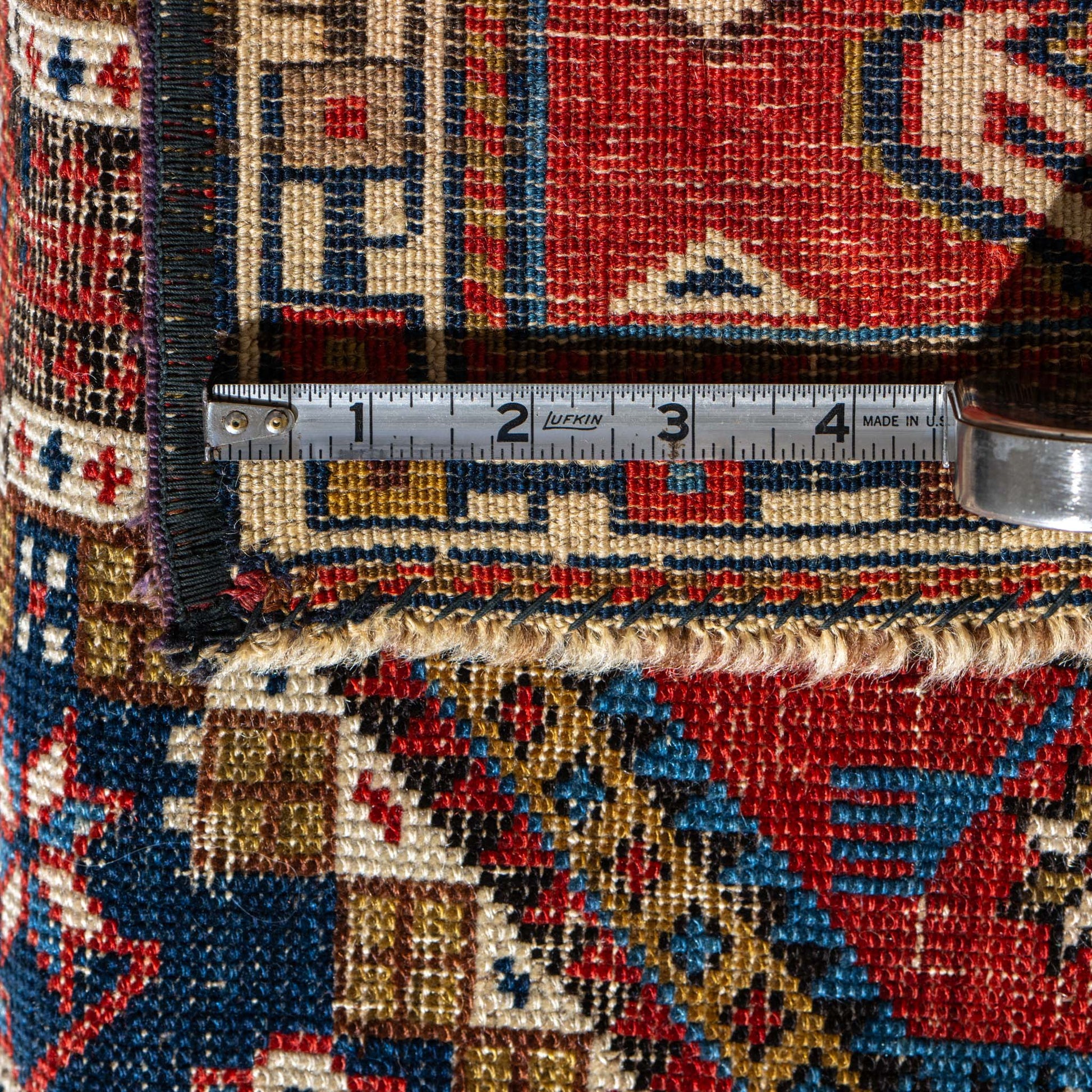 Close-up of a patterned rug with a measuring tape indicating dimensions.