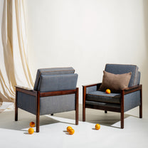 Two gray armchairs with wooden frames on a white floor with scattered oranges.