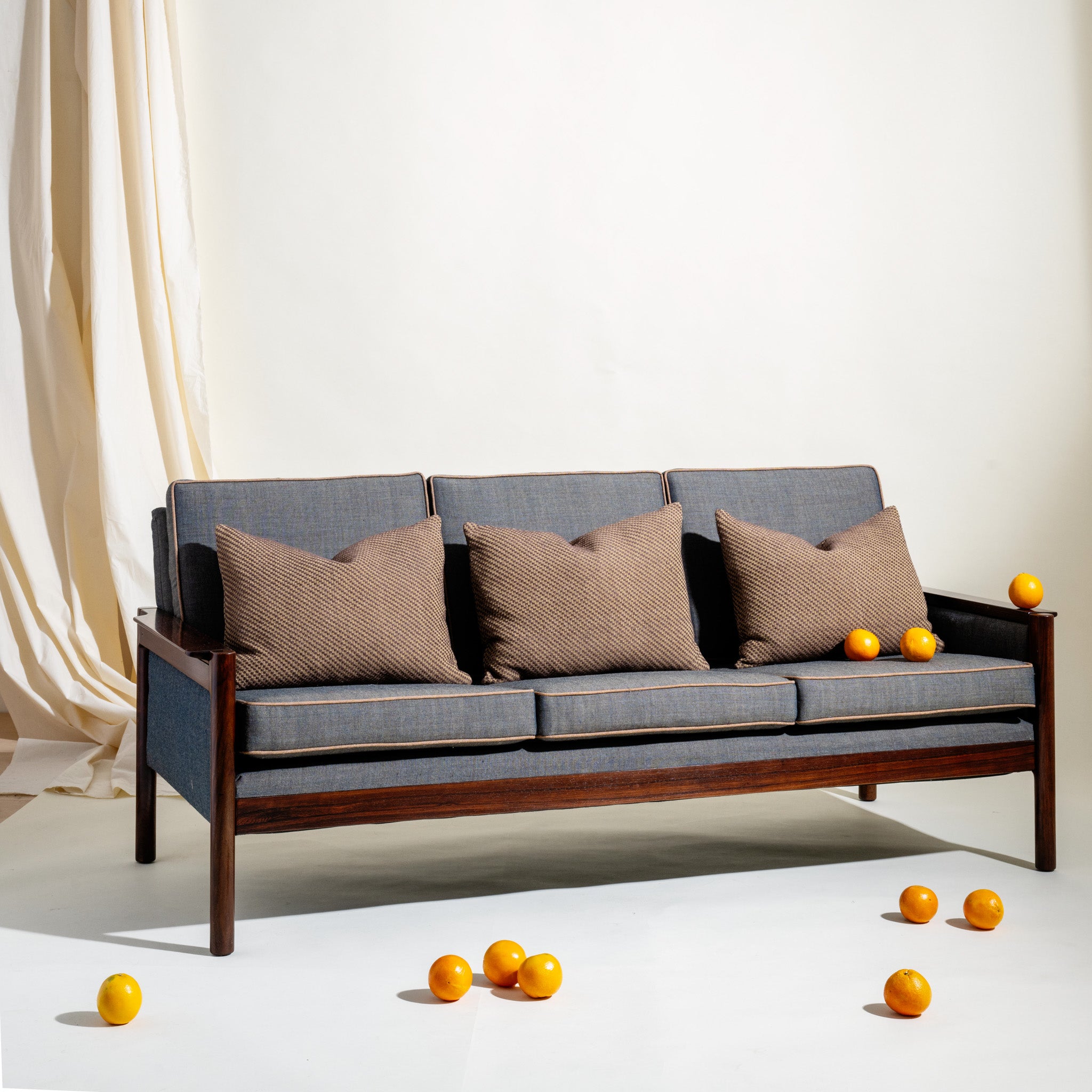 Gray Sven Ivar Dysthe sofa with wooden frame and brown cushions on a white floor with scattered oranges.