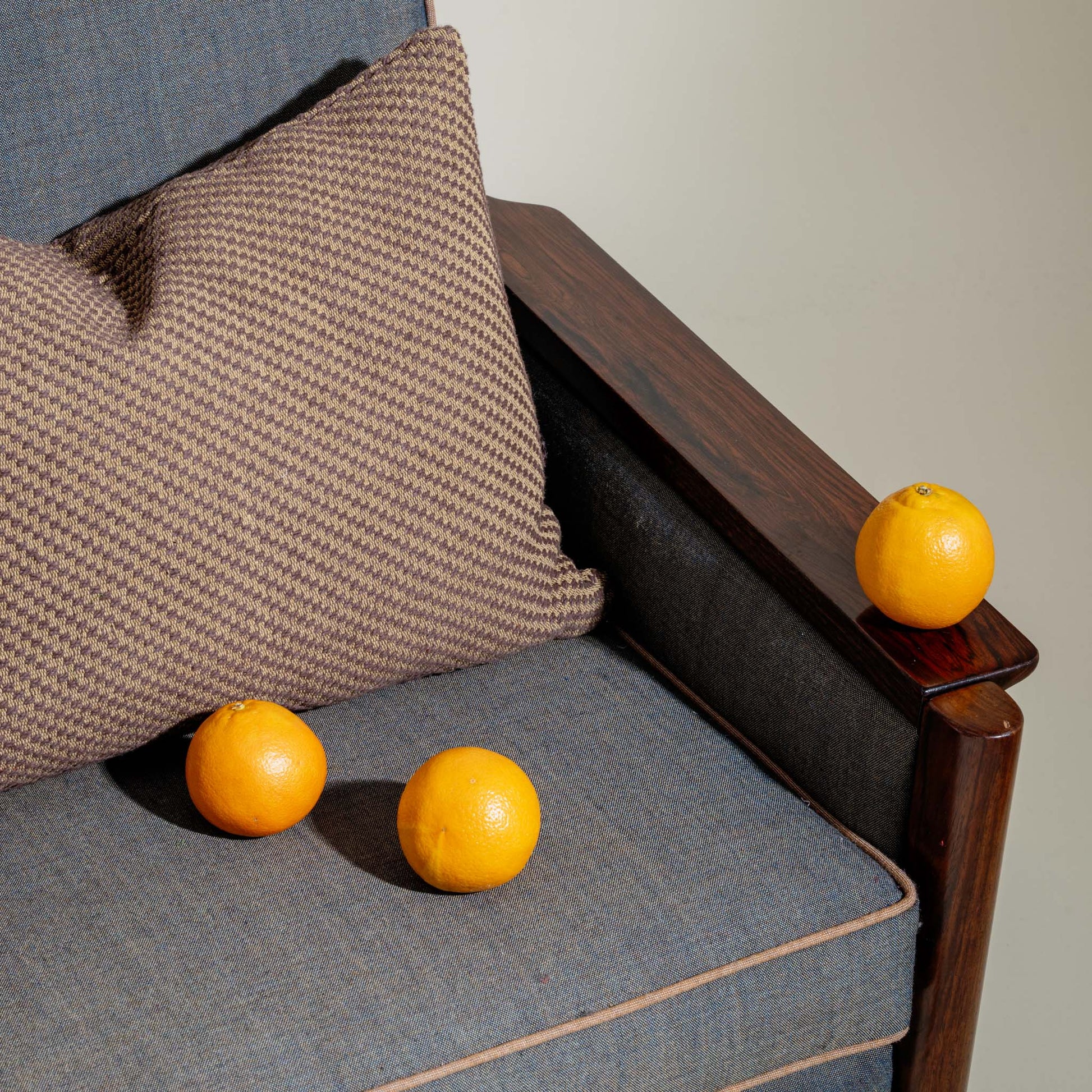 Oranges on a gray cushion of a wooden chair with a brown pillow.