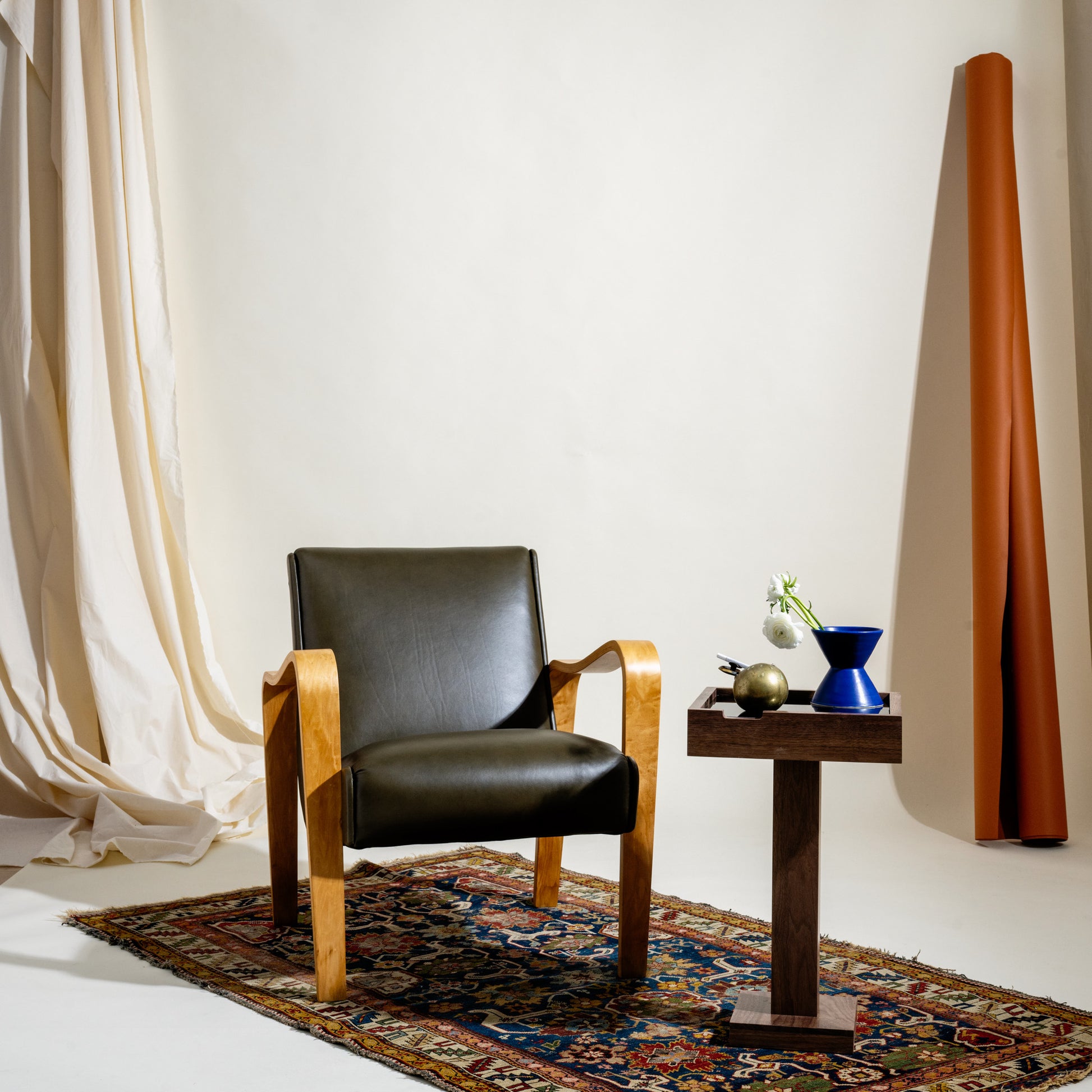 Dark olive leather chair with wooden frame next to a small table with decorative items on a patterned rug.