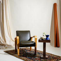 Dark olive leather chair with wooden frame next to a small table with decorative items on a patterned rug.