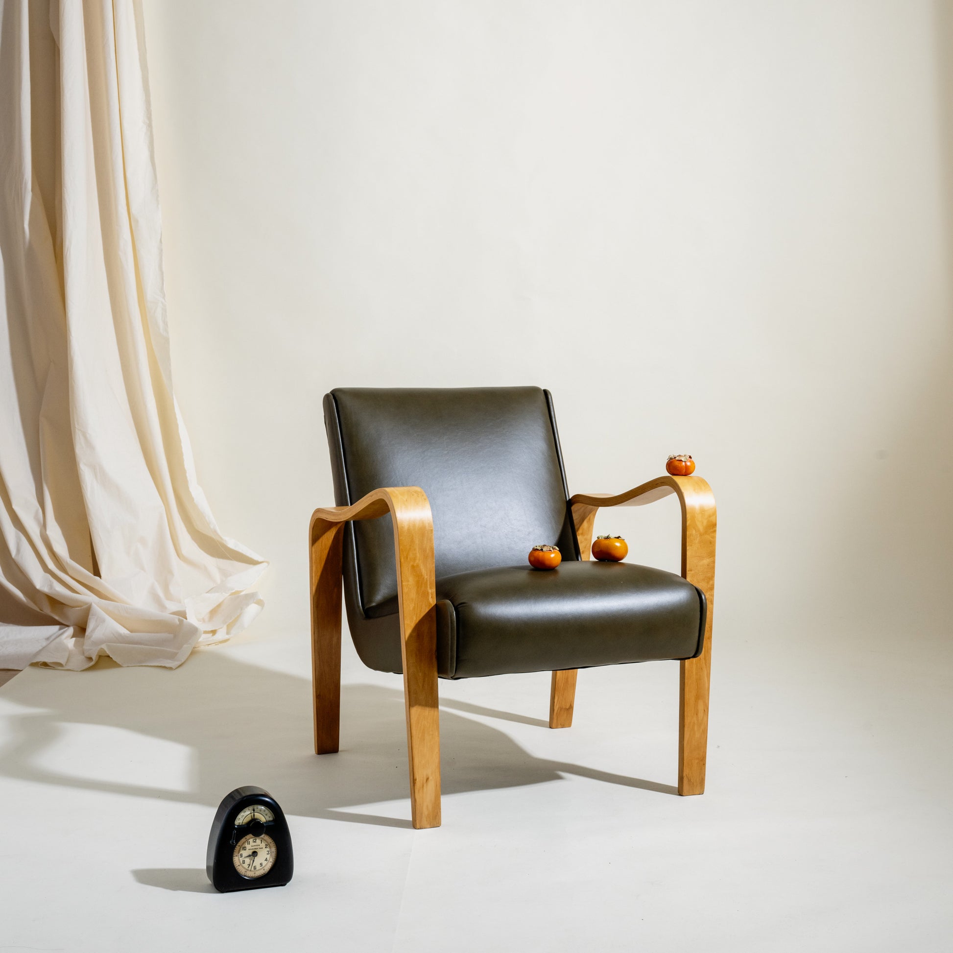 Modern armchair with deep olive 
leather seat and wooden frame against a white wall.