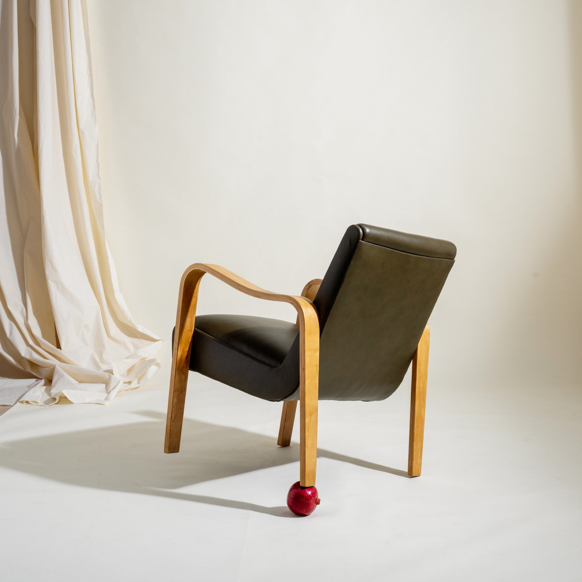 Modern chair with wooden frame and olive leather cushion against a white background