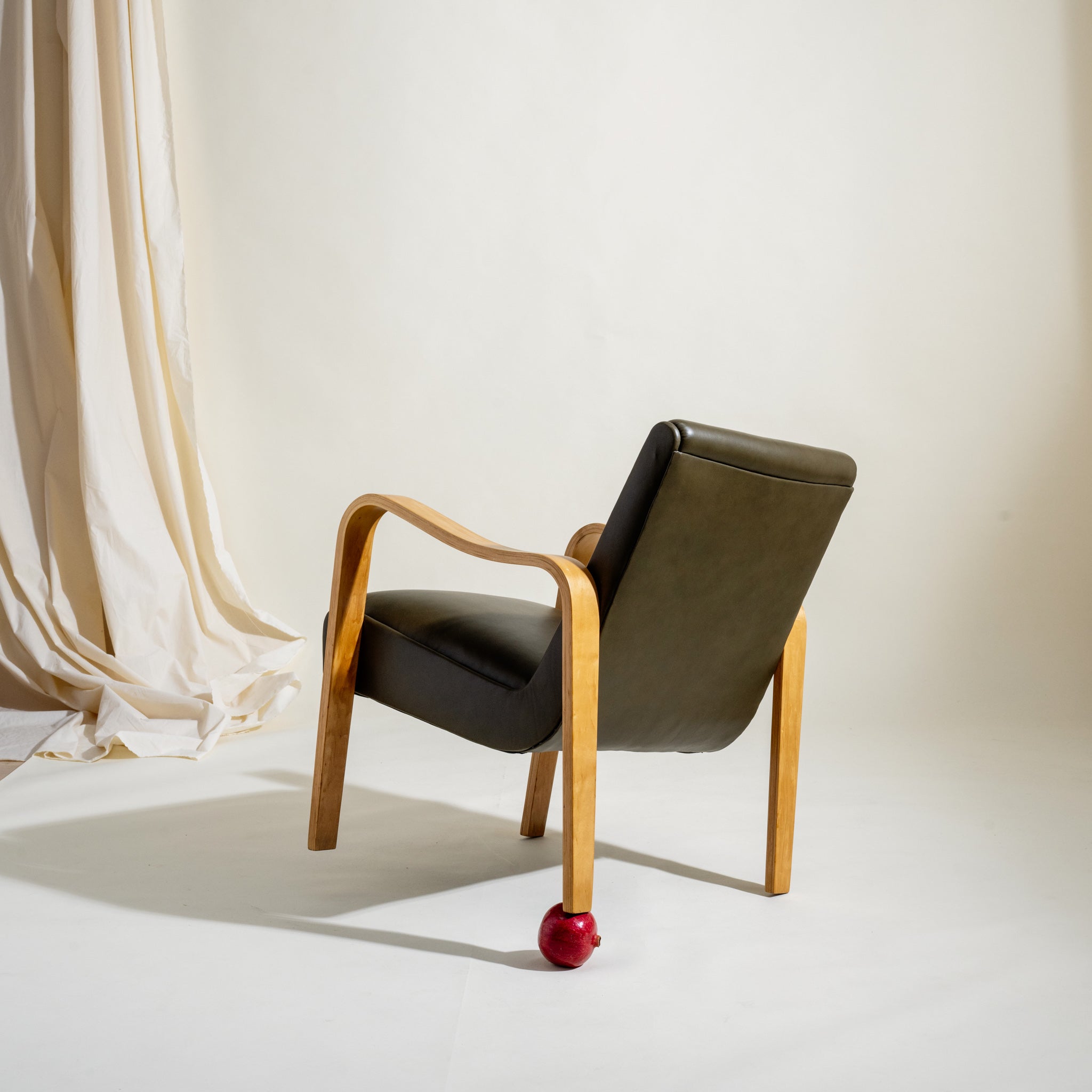 Modern chair with wooden frame and olive leather cushion against a white background