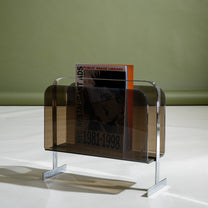 Metallic magazine holder with books on a white surface and green background