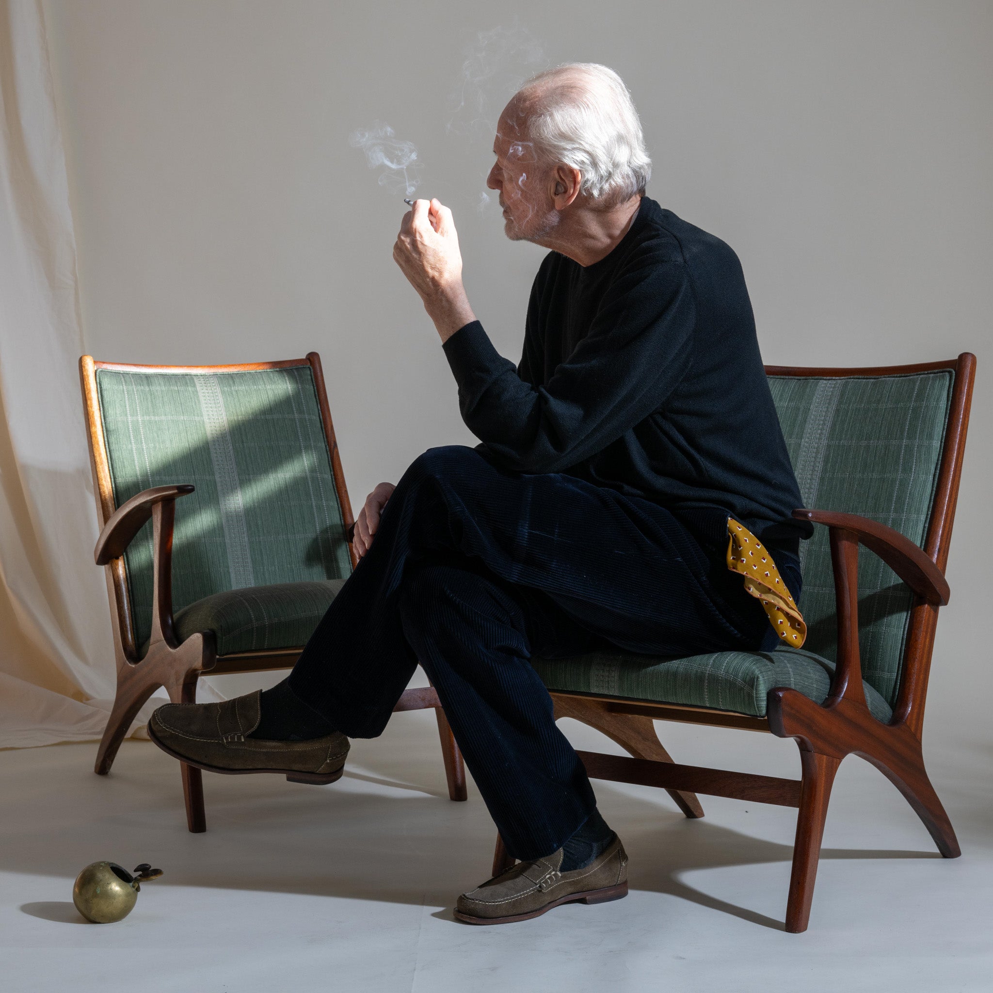 Man sitting in a chair smoking a cigarette with a minimal background