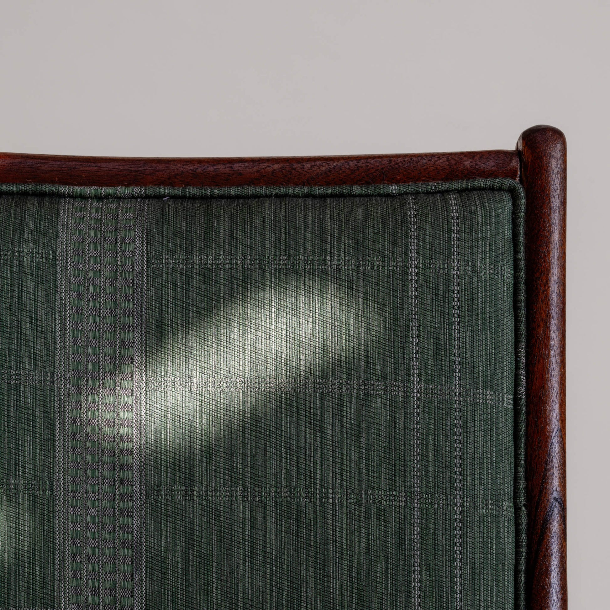 Close-up of the green fabric surface on the chair with the wooden frame details surrounding it