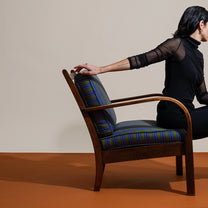 Person  with their arm outstretched resting on a wooden armchair with striped cushions on a beige and brown background