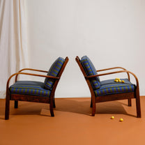 Two wooden Frits Schlegel armchairs with striped cushions on a brown floor and white wall background.