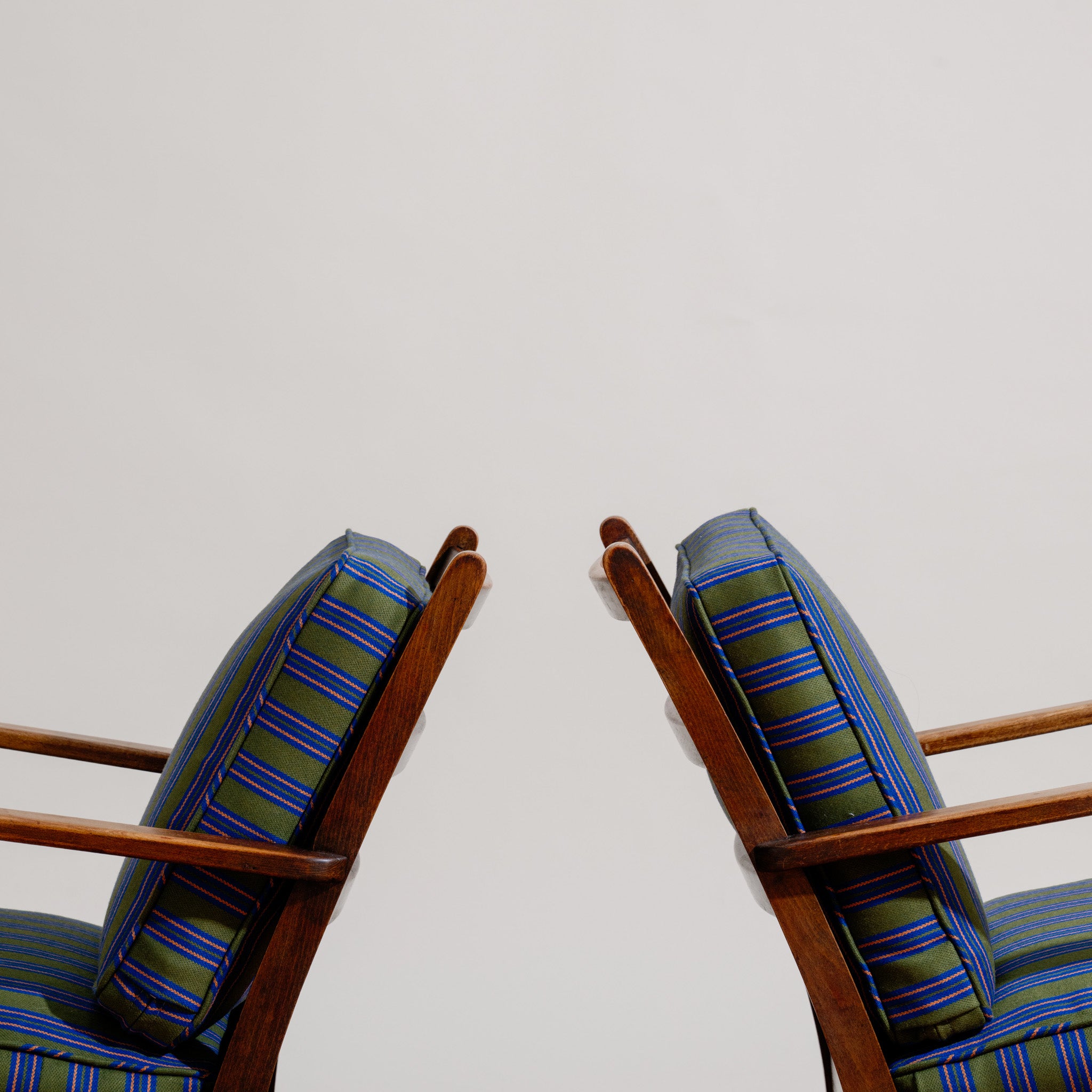 Two wooden Frits Schlegel chairs with striped cushions on a plain background