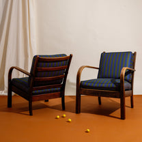 Two wooden Frits Schlegel chairs with blue striped cushions on an orange floor.