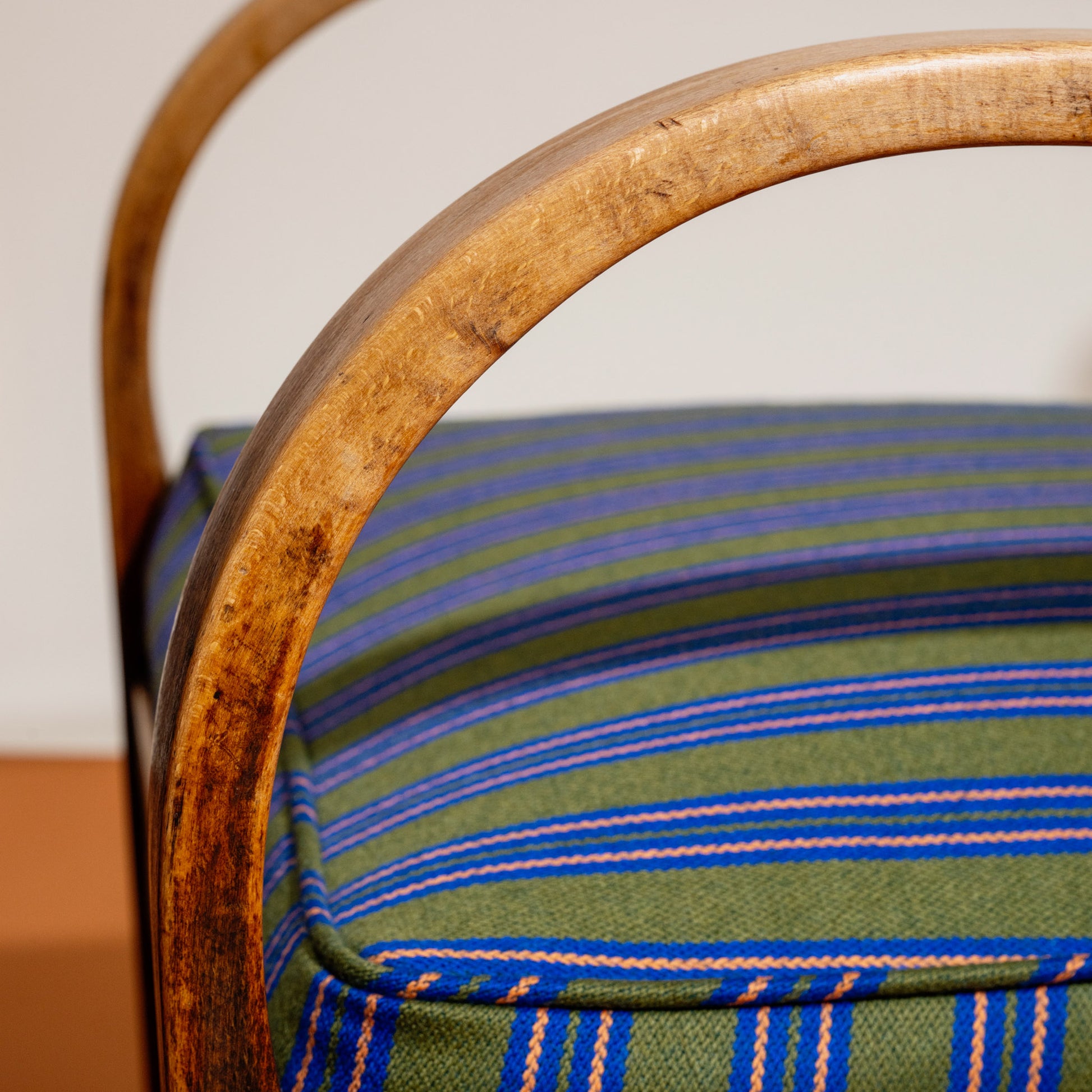 Close-up of a chair's with wooden armrests with striped green and blue Nobilis fabric cushion in the background.