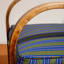 Close-up of a chair's with wooden armrests with striped green and blue Nobilis fabric cushion in the background.