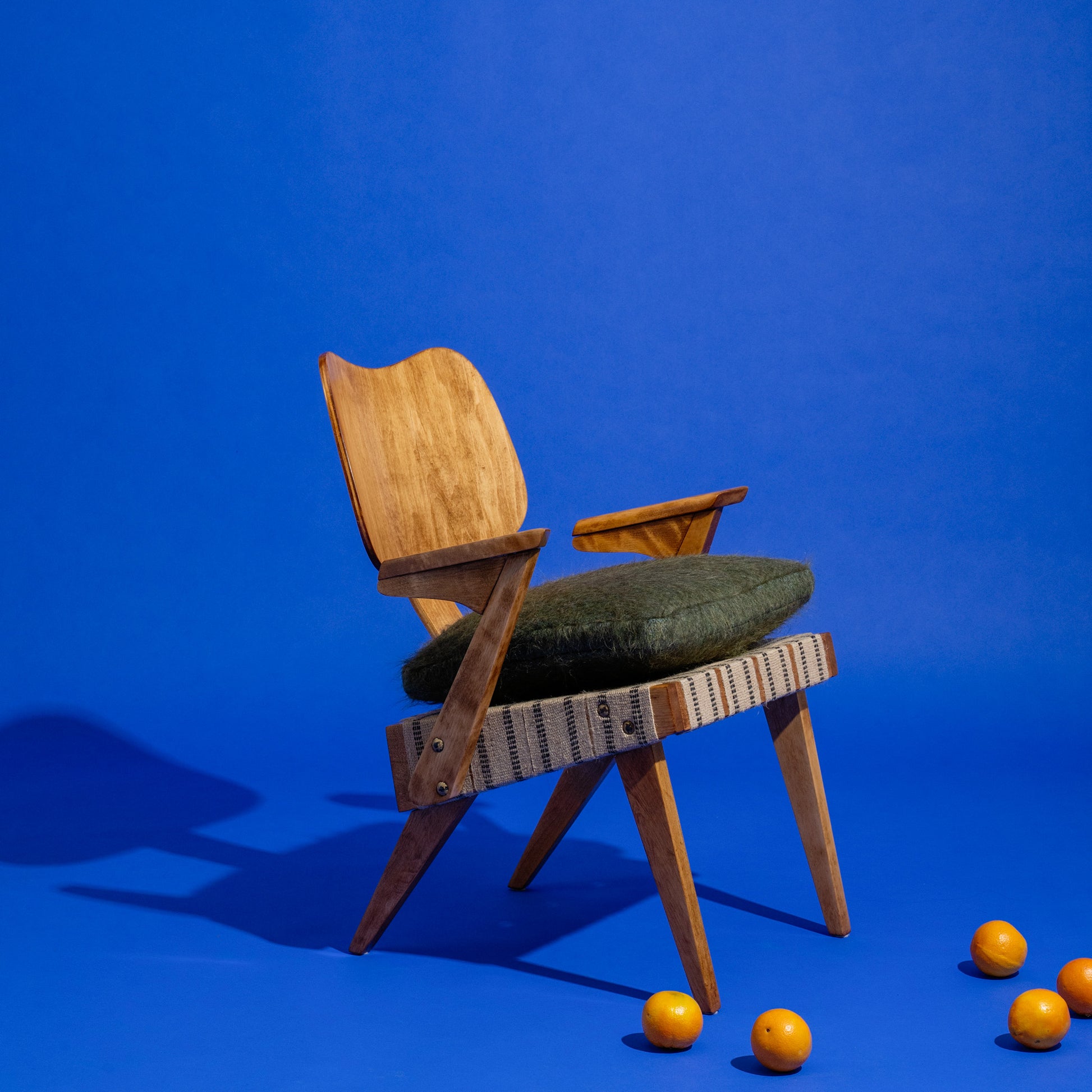 Wooden Russell Spanner “Ruspan” chair with green cushion on a blue background with oranges around