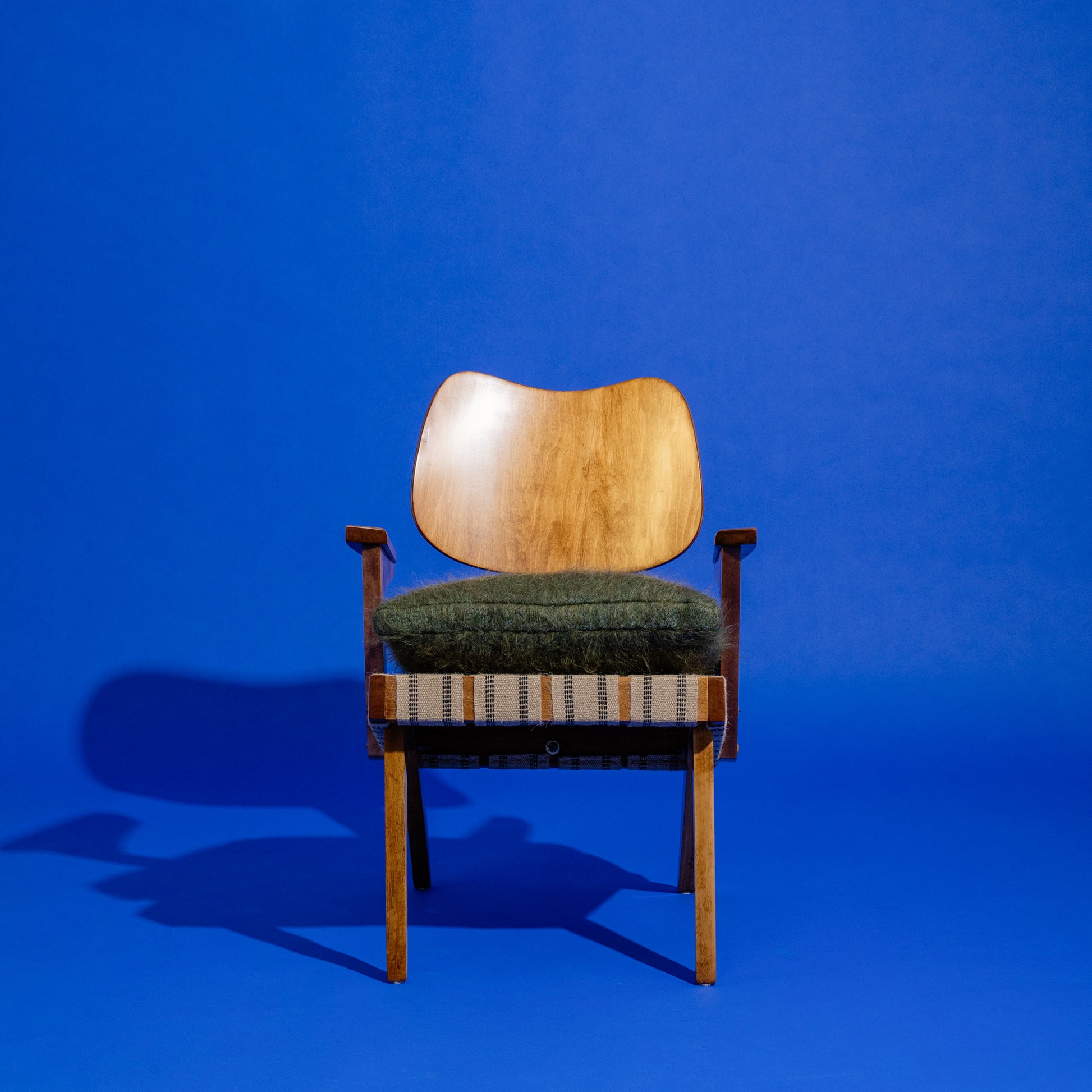 Wooden Russell Spanner chair with green cushion on a blue background
