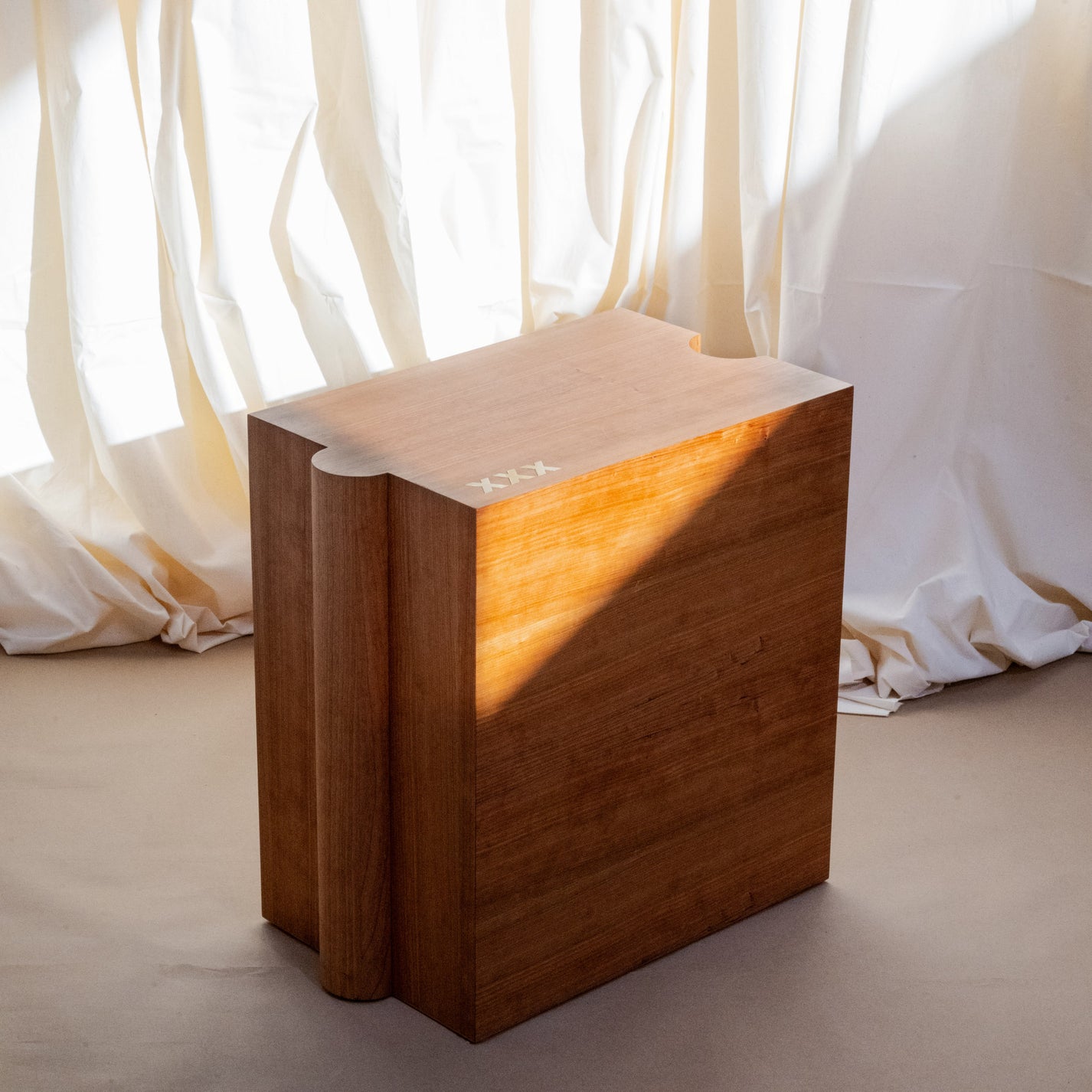 Handmade Wooden table with a textured surface against a white curtain background. The table has a puzzle like shape with delicate craftsmanship and three inlaid X's at the front left corner.