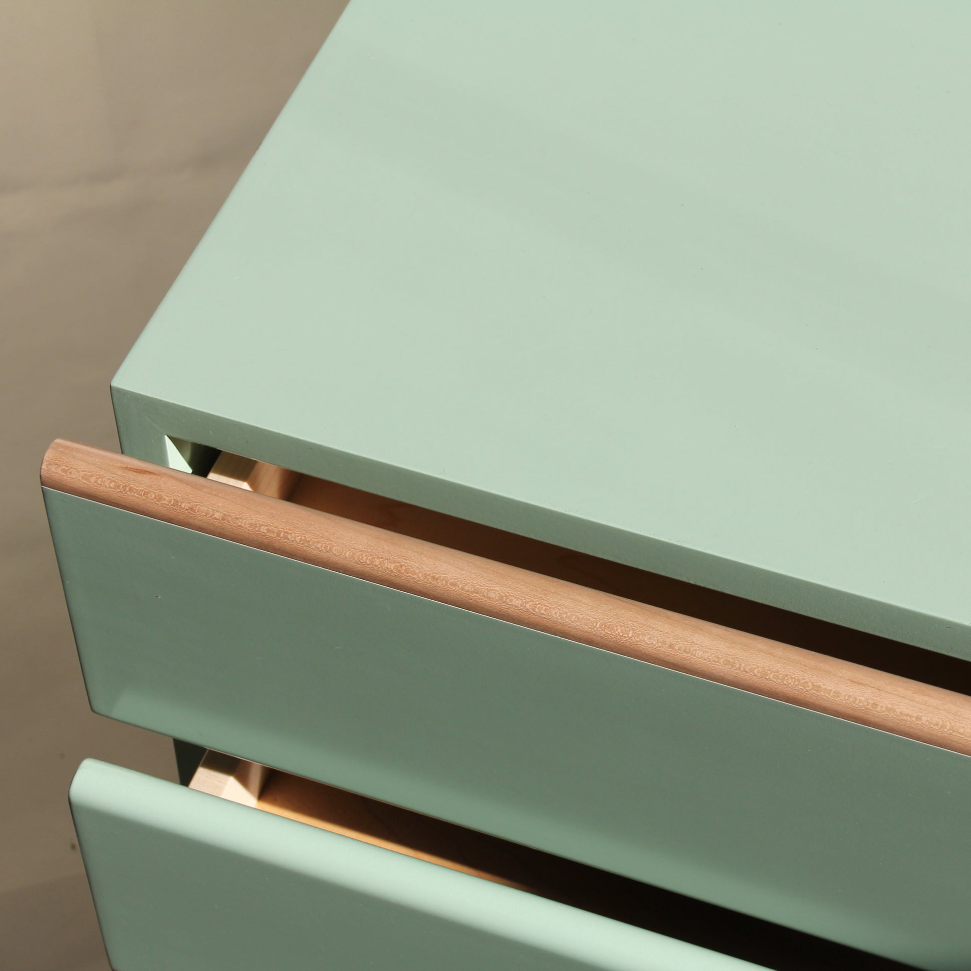 Close-up of a green drawer with wooden handles on a beige background. Beautiful detailing on a handmade wood nightstand.