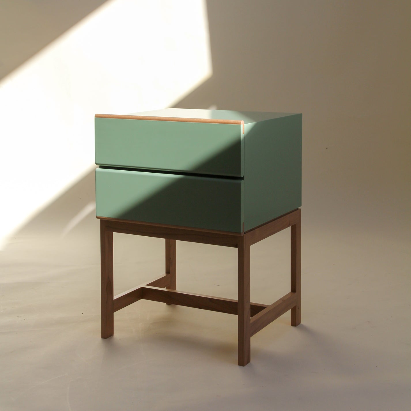 Elegant handcrafted green nightstand with wooden legs on a neutral background.