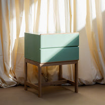 Elegant Wooden nightstand with a two drawer rectangular top section that is painted Farrow &amp; Ball Breakroom Green. The nightstand is open at the base with small wooden rectangular legs. There are four legs coming down from each corner with one parallel wooden piece toward the bottom half and one wooden piece at the same height at the bottom going across the space horizontally.