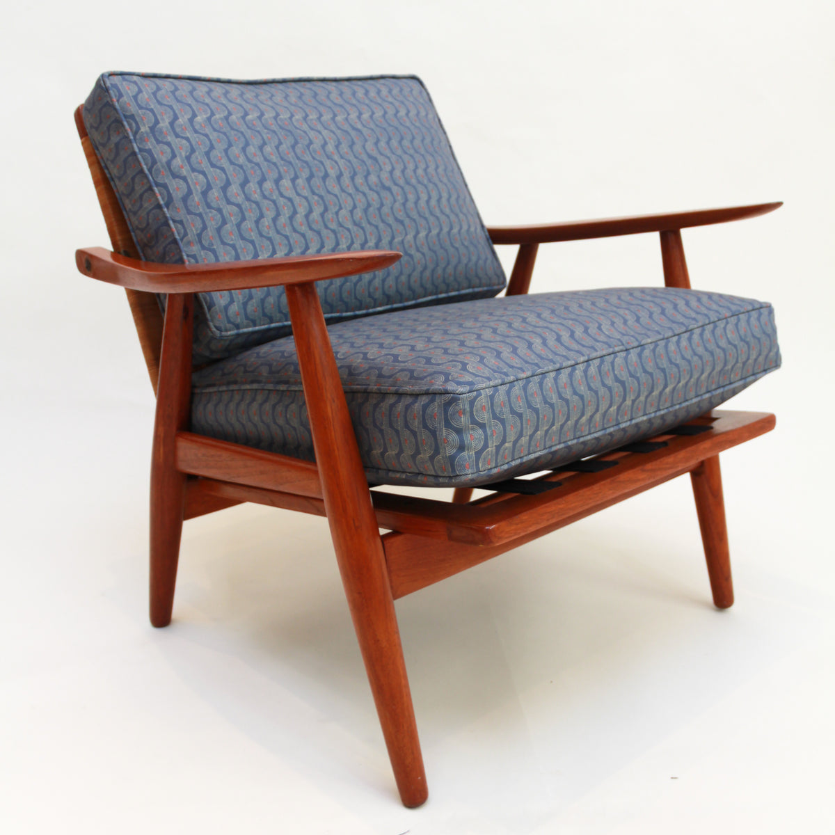Wooden Hans Wegner armchair with blue patterned cushions on a white background