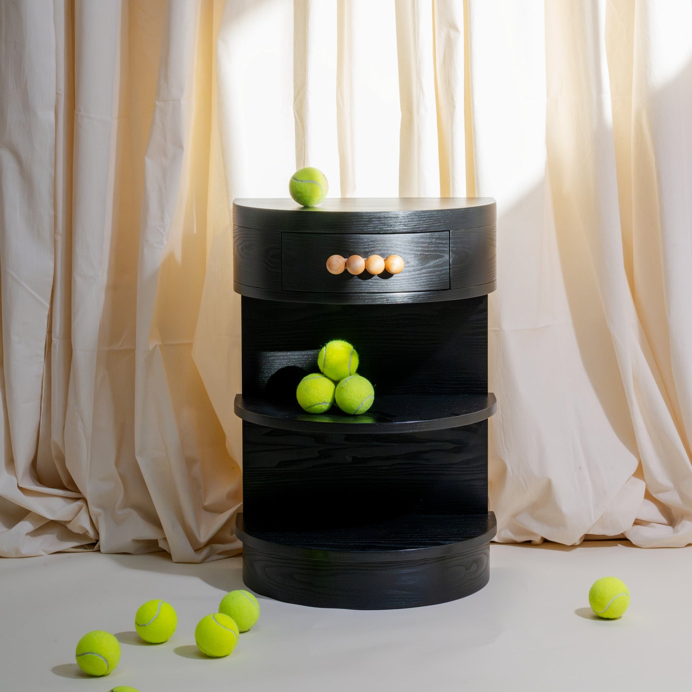 A black demi-lune nightstand styled with tennis balls on a light background