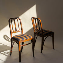 Two wooden chairs with striped cushions on a plain background