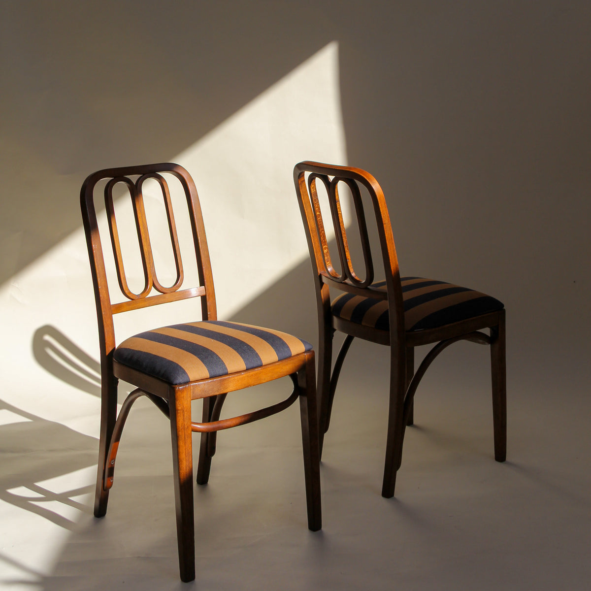 Two wooden chairs with striped cushions on a plain background