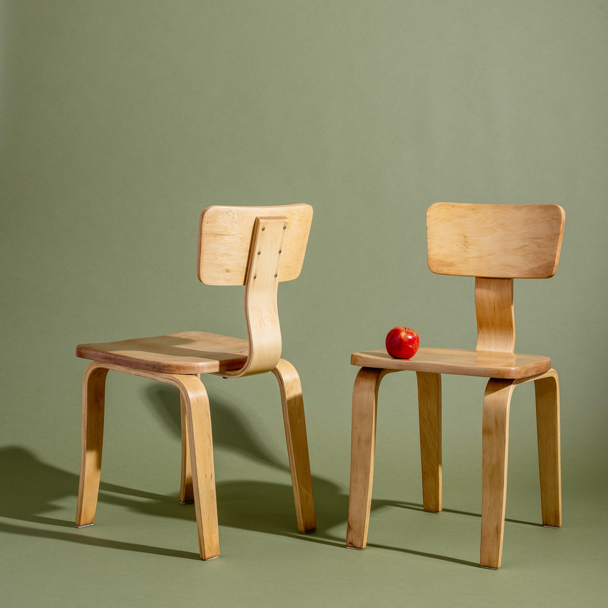 Two wooden chairs on a green background with a red apple on one chair.