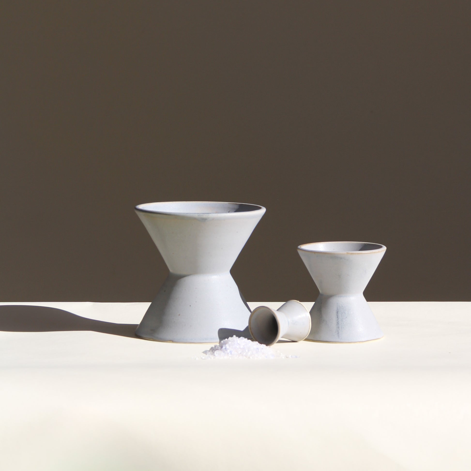 Three ceramic vessels on a white table with a darker background