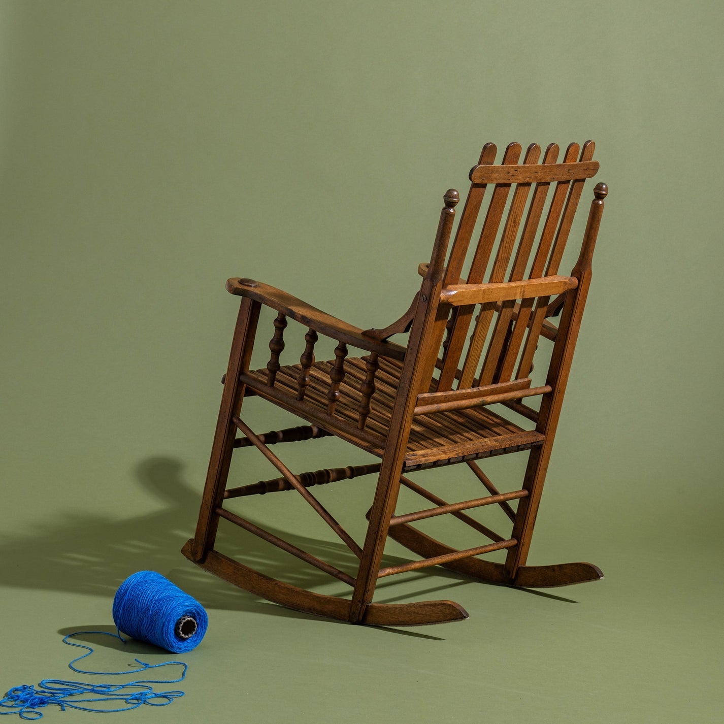 Wooden rocking chair on a green background with a ball of blue yarn.