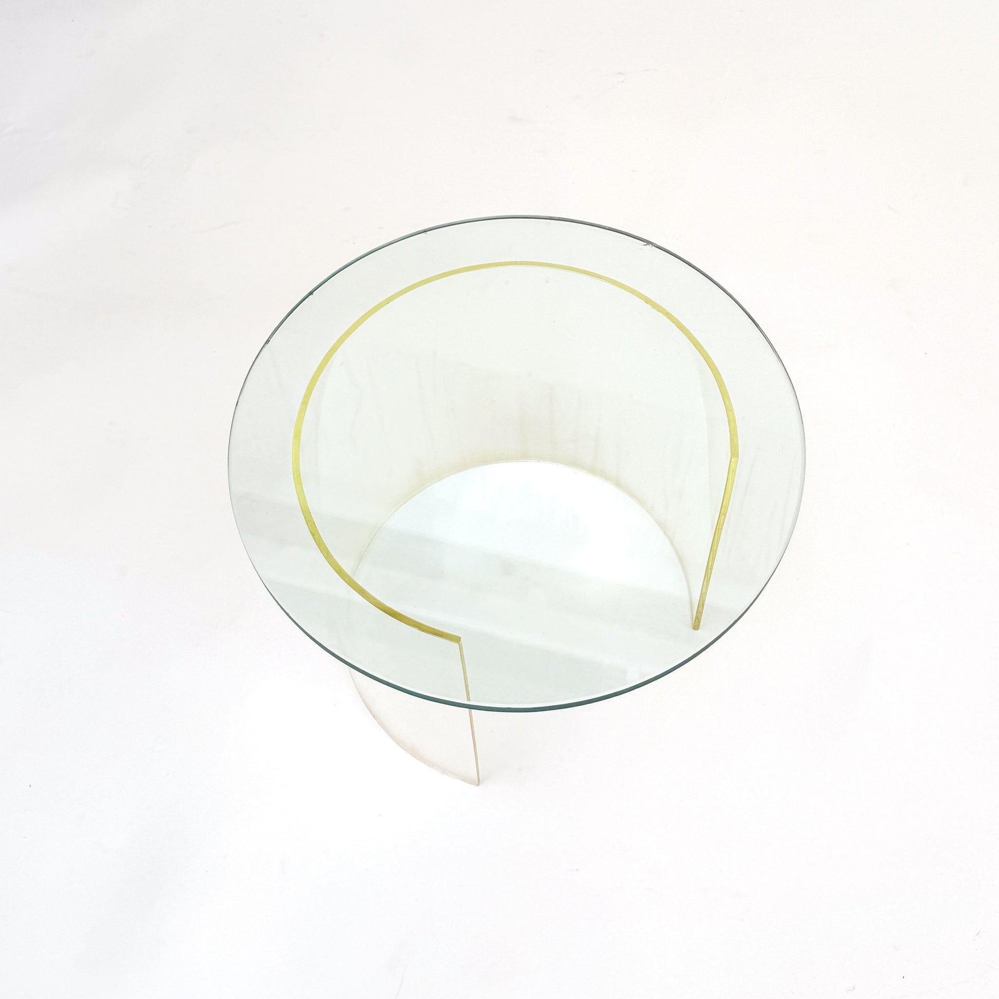 A modern round glass coffee table with a clear glass top and a sculptural, curved clear base, photographed from a top-down angle on a white background.